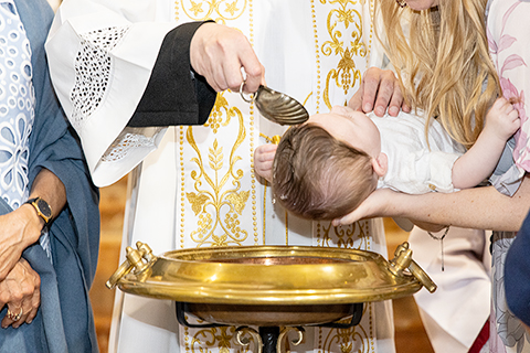Sacerdote versa l’acqua sulla testa del neonato durante il rito del battesimo a Milano