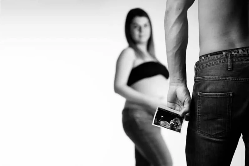Coppia in attesa con simboli matematici e pancione in evidenza su sfondo nero