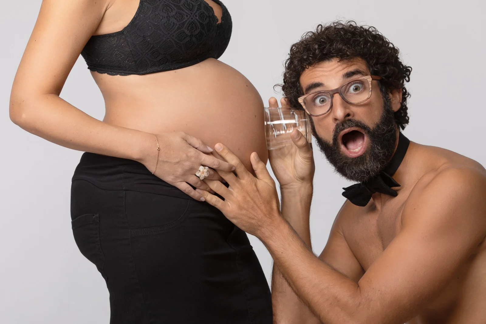 Papà divertito ascolta la pancia della futura mamma durante shooting gravidanza