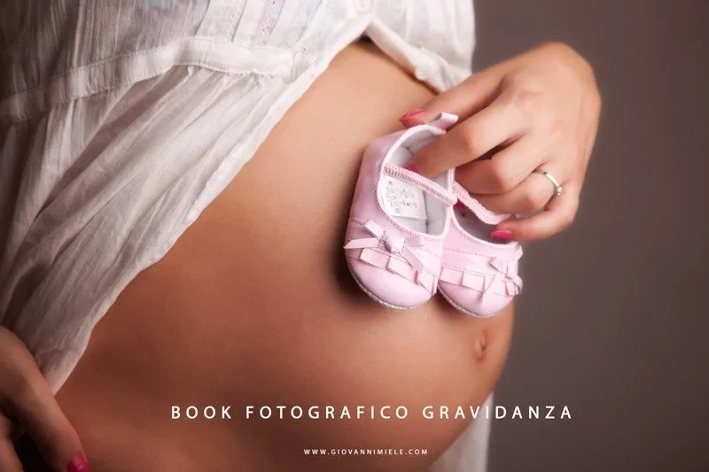 Primo piano di una pancia incinta con scarpette rosa da neonato