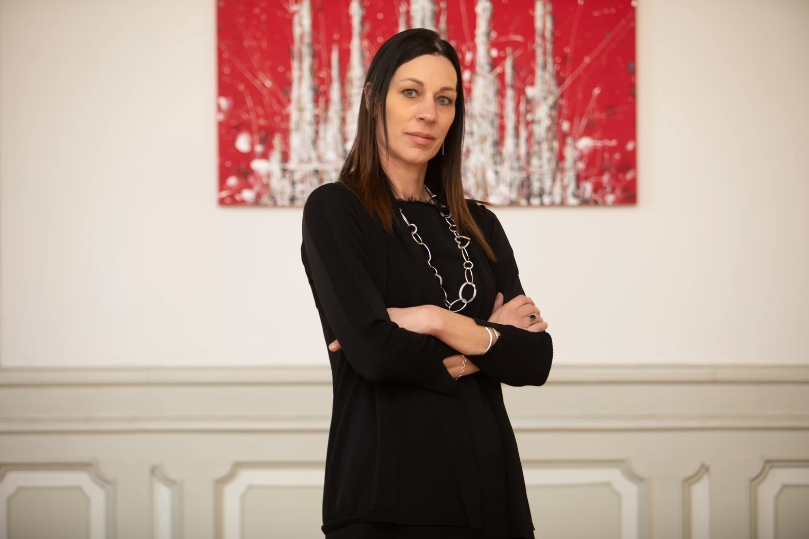 Foto del team aziendale in ufficio: ritratto di una donna in abito nero davanti a un quadro rosso, su una parete con boiserie chiara